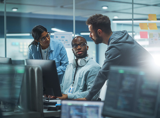 Three cybersecurity professionals consult while sitting in front of a computer.