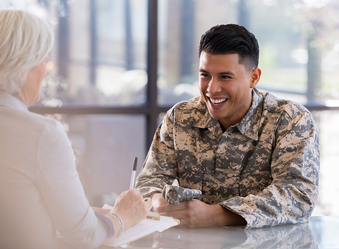 A man in a military uniform sits at a table across from an advisor.