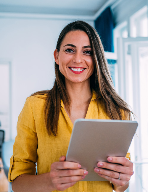 A woman stands in an office and looks over cybersecurity courses on a tablet.