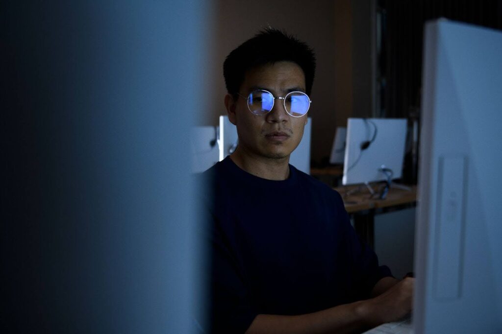 A male student wearing glasses looks at a screen in a computer lab.