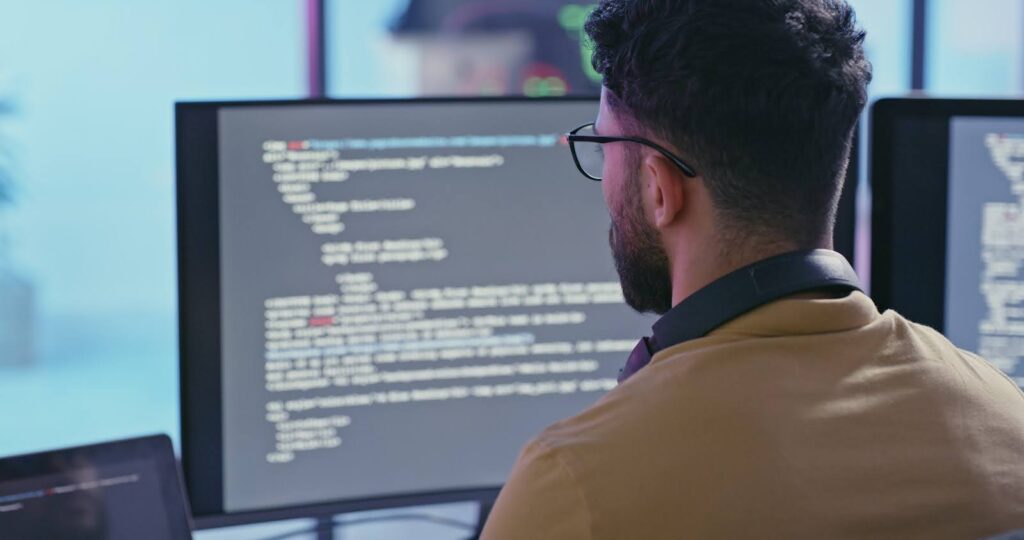 A cybersecurity professional writes cybersecurity analytics code at a multi-screen workstation.